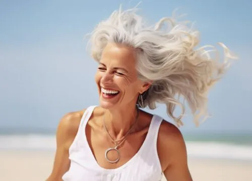 Photo of a happy older woman on the beach wearing a white top