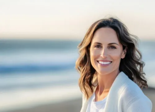 Serene smile of a 40-year-old woman in light colors and sky blue sweater on the beach.